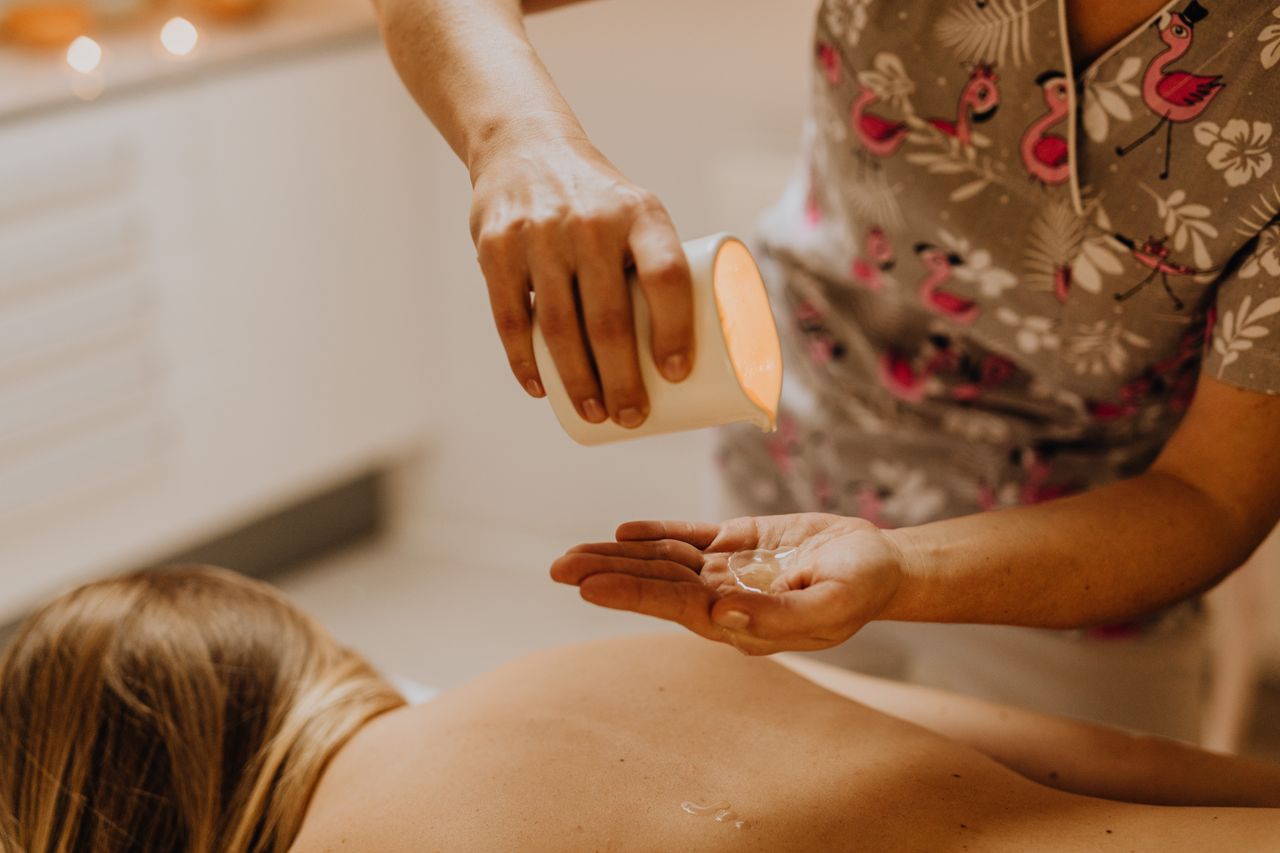 Close-up of a masseuse pouring massage oil during a relaxing spa session indoors.